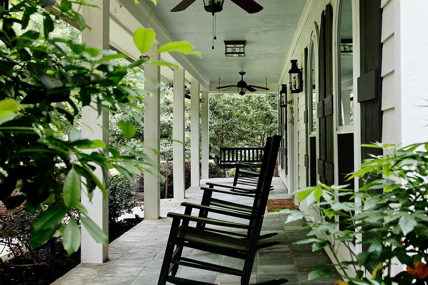 Deep covered front porch with rocking chairs and garden views