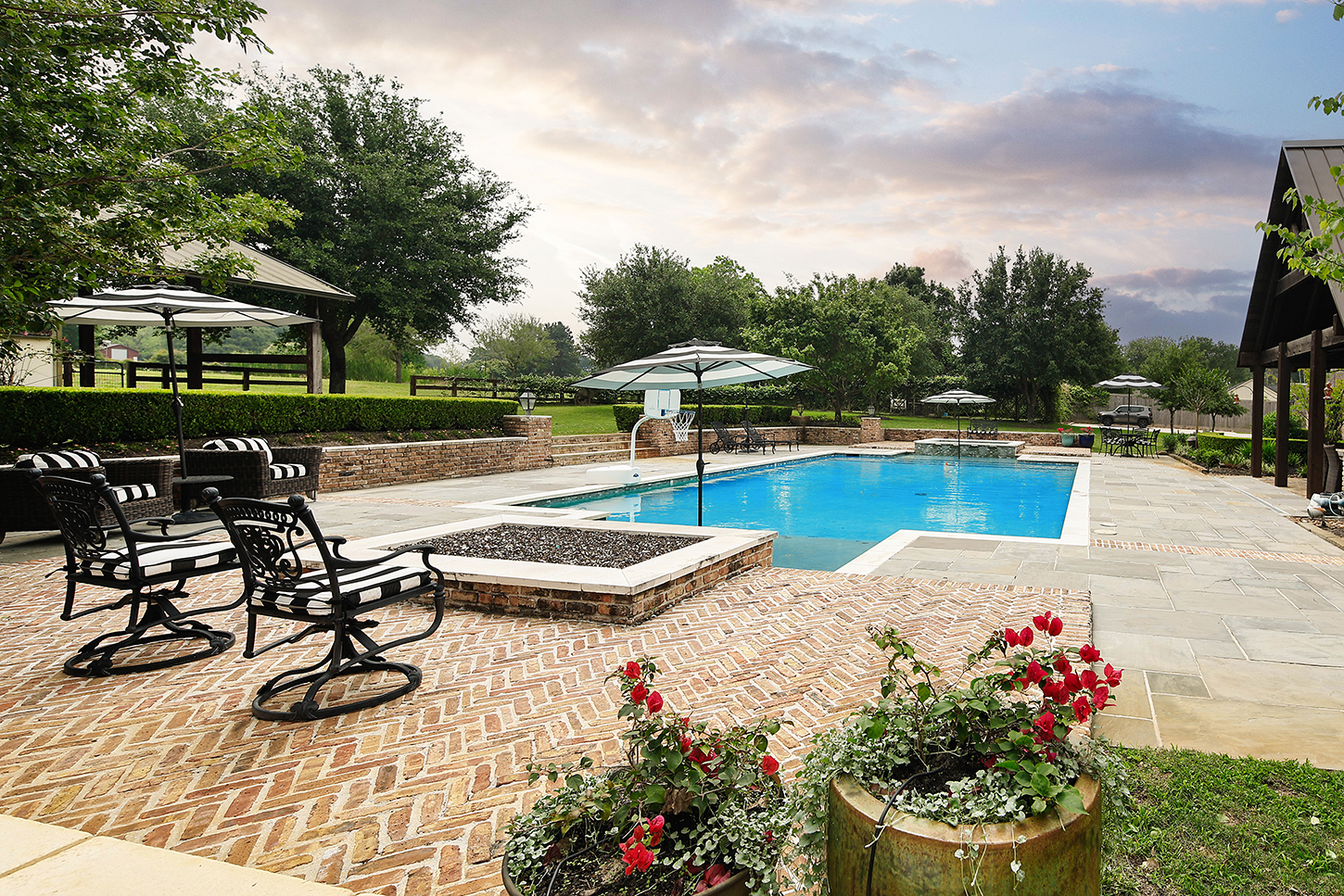 Pool deck with brick firepit and umbrellas at sunset