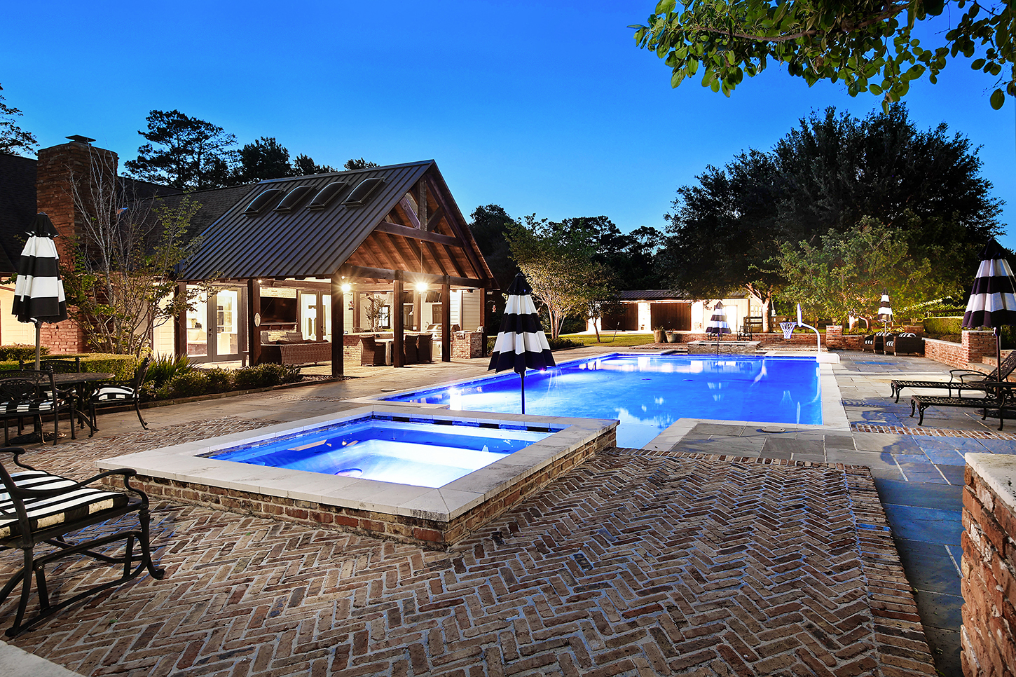 Pool and lit pavilion with outdoor kitchen at twilight