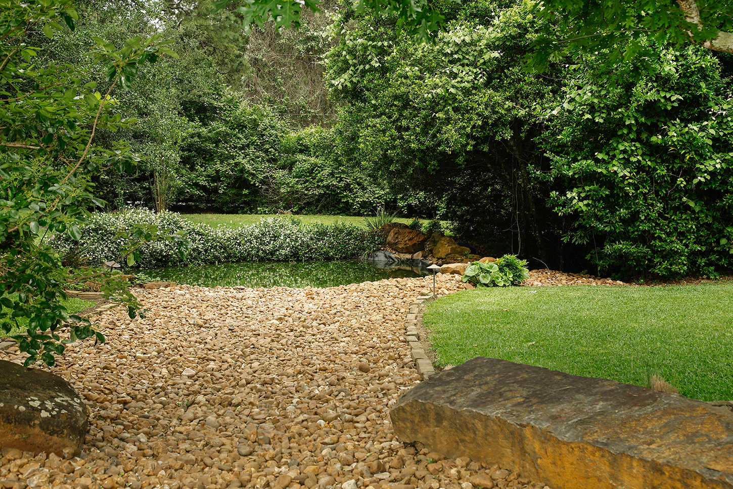 Stone-lined dry creek bed bordered by lawn and mature trees