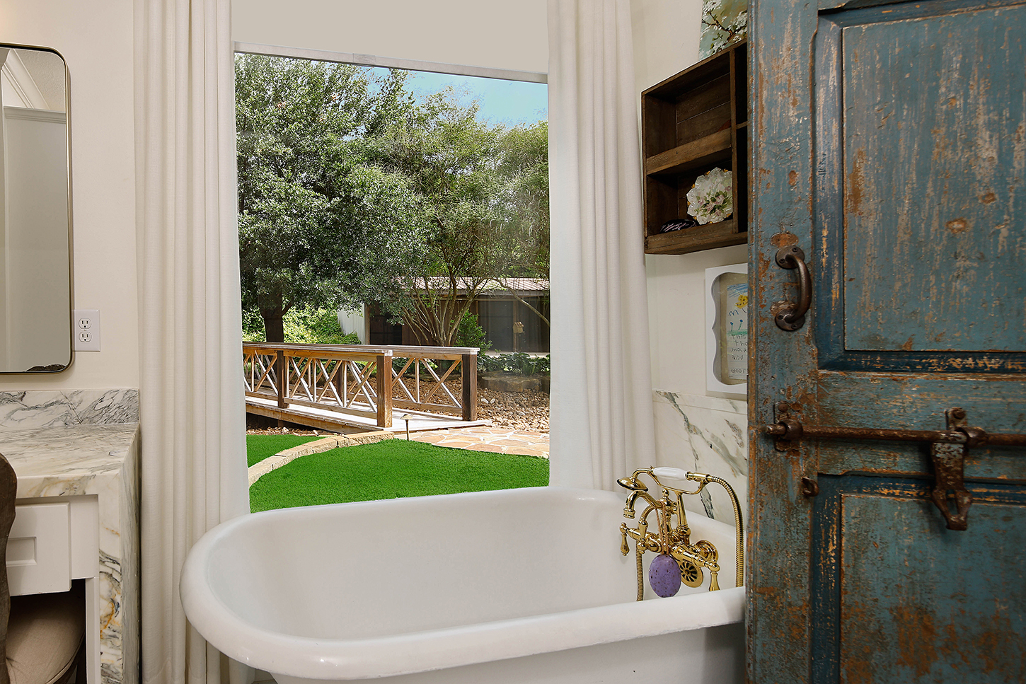 Primary bath with clawfoot tub, antique blue doors, and garden view
