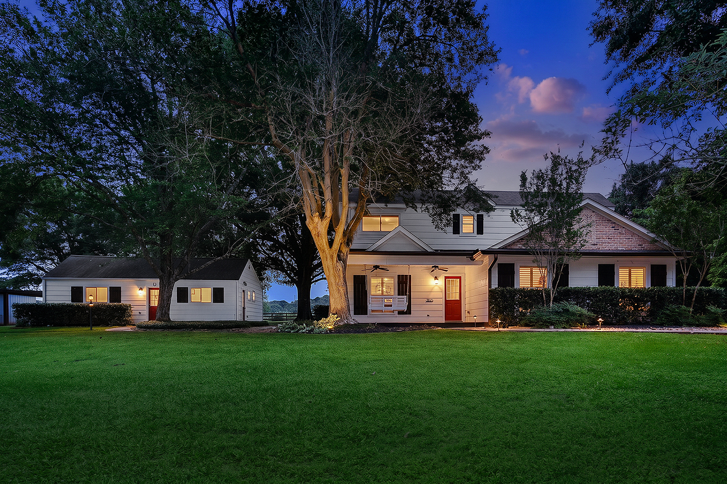 Main house front porch with swing at twilight beneath mature trees